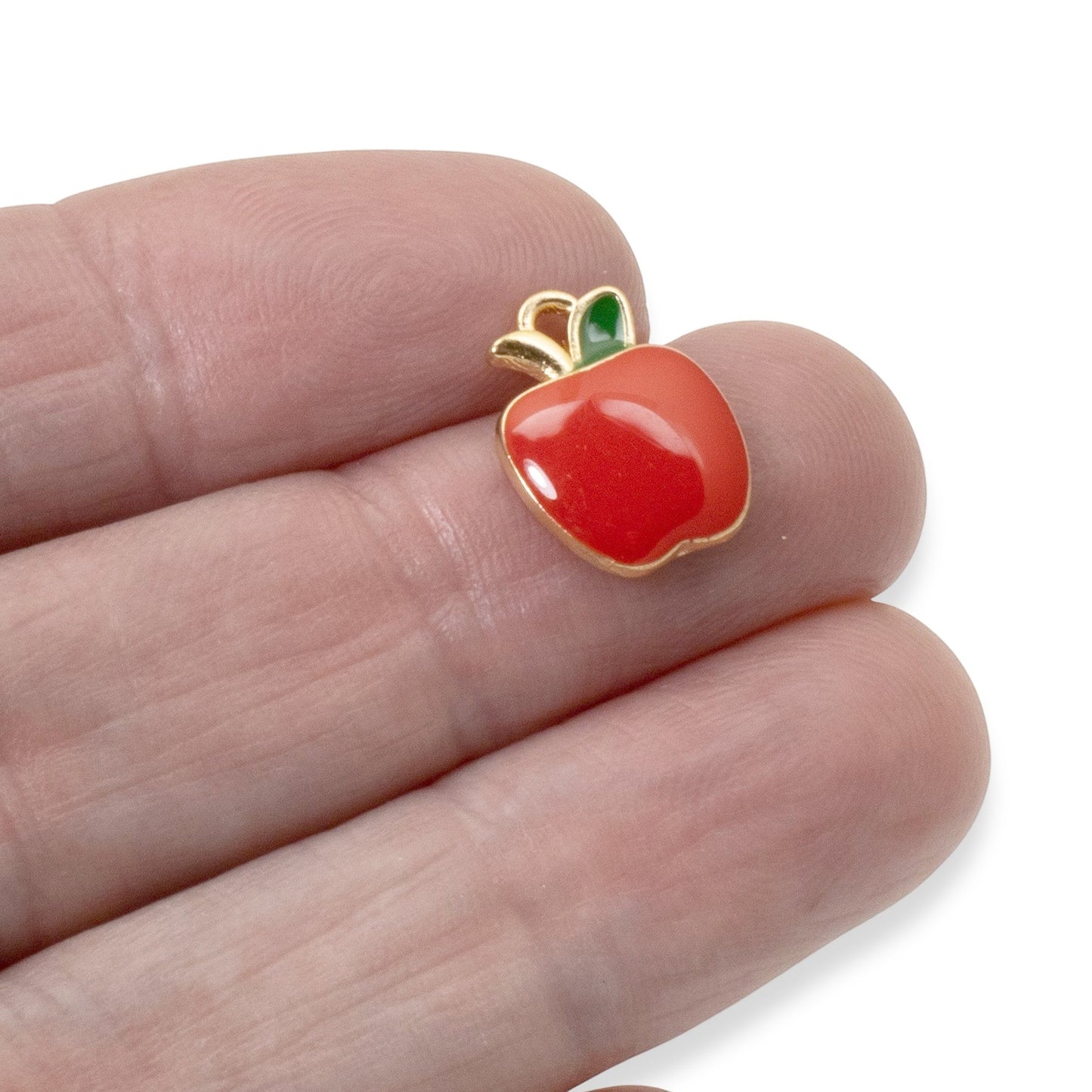 Hackberry Creek glossy red enamel apple charm with a green leaf and gold trim held between fingers