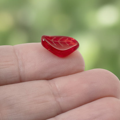 Hackberry Creek transparent Siam red Czech glass leaf bead with intricate veining detail held on a fingertip