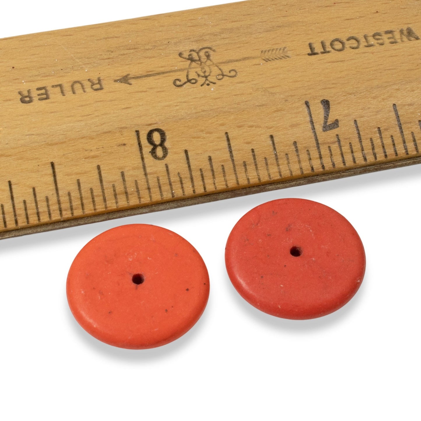 Hackberry Creek muted red magnesite stone rondelle disk beads next to a wooden ruler for size reference
