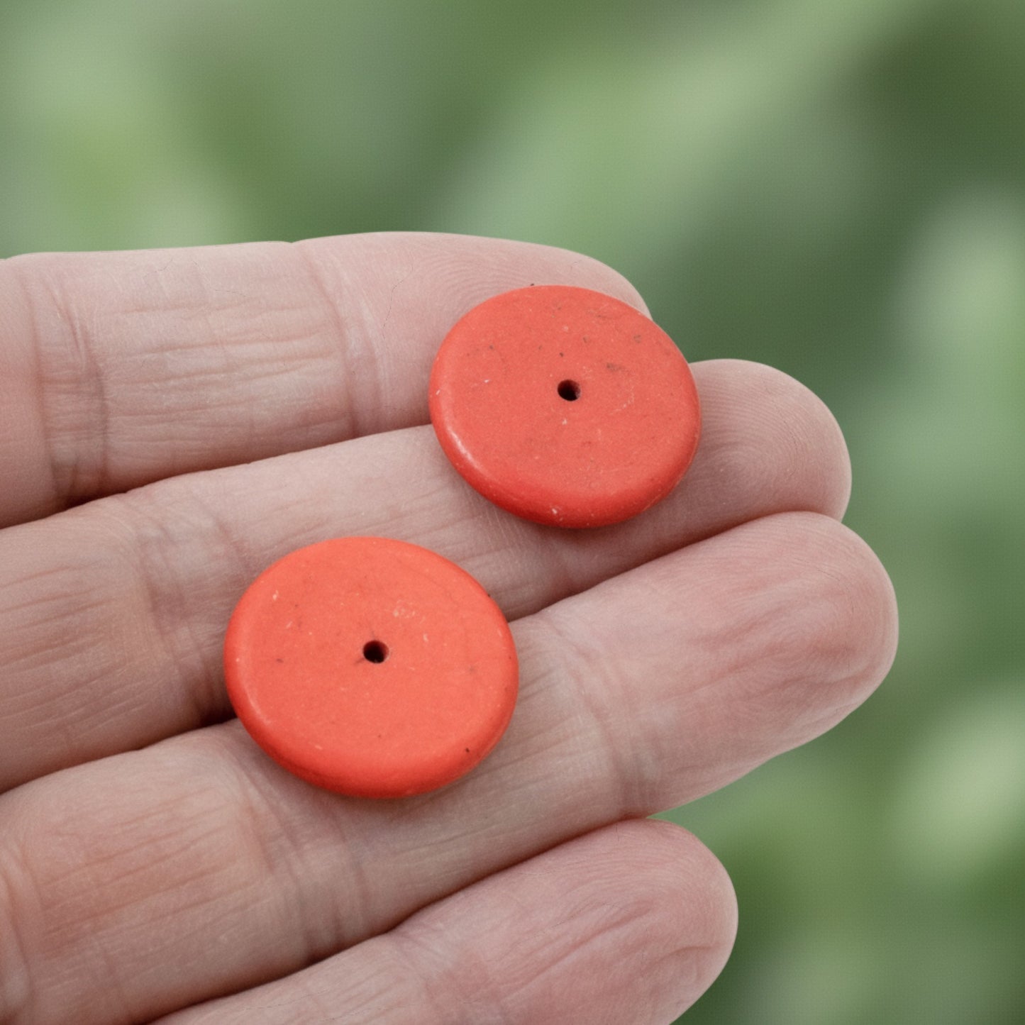 Hackberry Creek muted red magnesite stone rondelle disk beads held in a hand for jewelry making