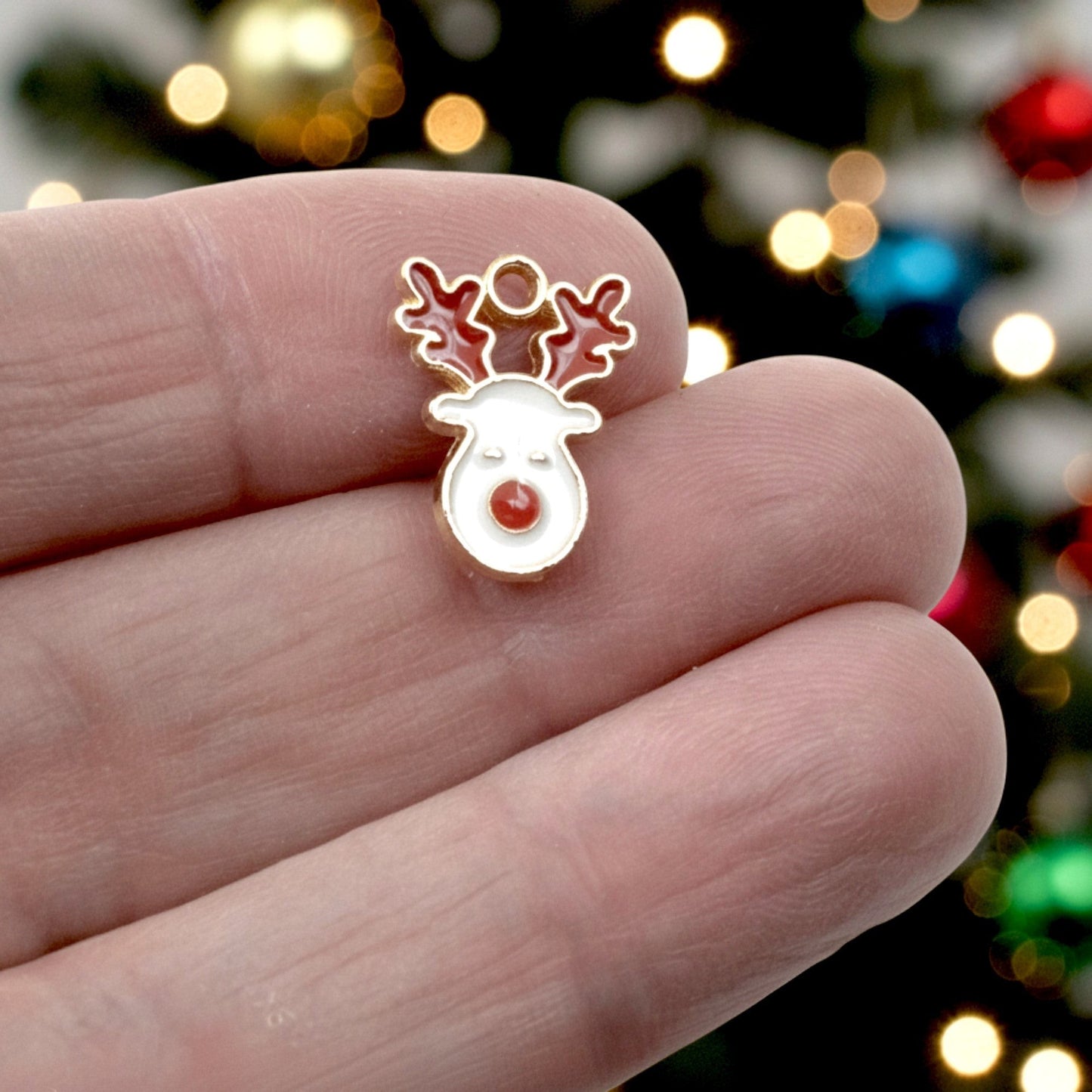 Hackberry Creek reindeer face charm with white enamel, red nose, and red antlers on a gold-plated base held in hand.