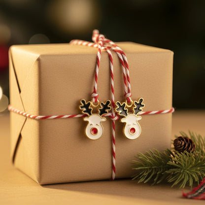 Hackberry Creek reindeer enamel charms with red noses and black antlers tied to a brown gift box with festive twine.