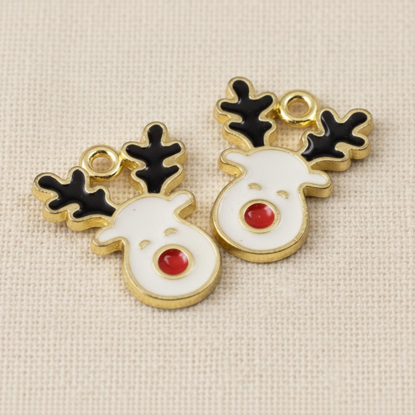Hackberry Creek reindeer enamel charms with white faces, red noses, and black antlers on gold-plated metal bases.