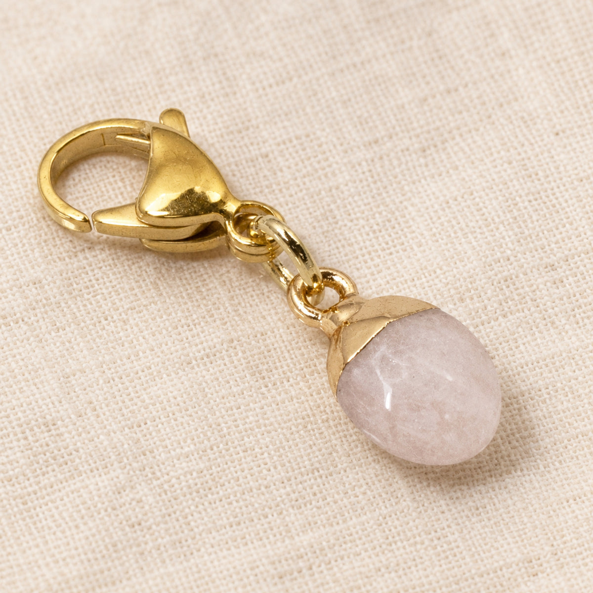 Hackberry Creek dainty oval rose quartz charm with a gold-plated stainless steel lobster clasp on textured fabric