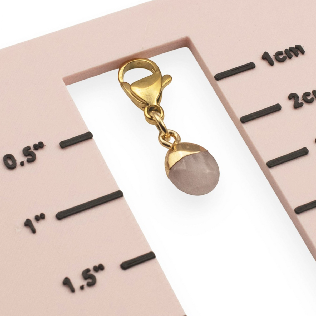 Hackberry Creek dainty oval rose quartz charm with a gold-plated stainless steel clasp on a measurement scale