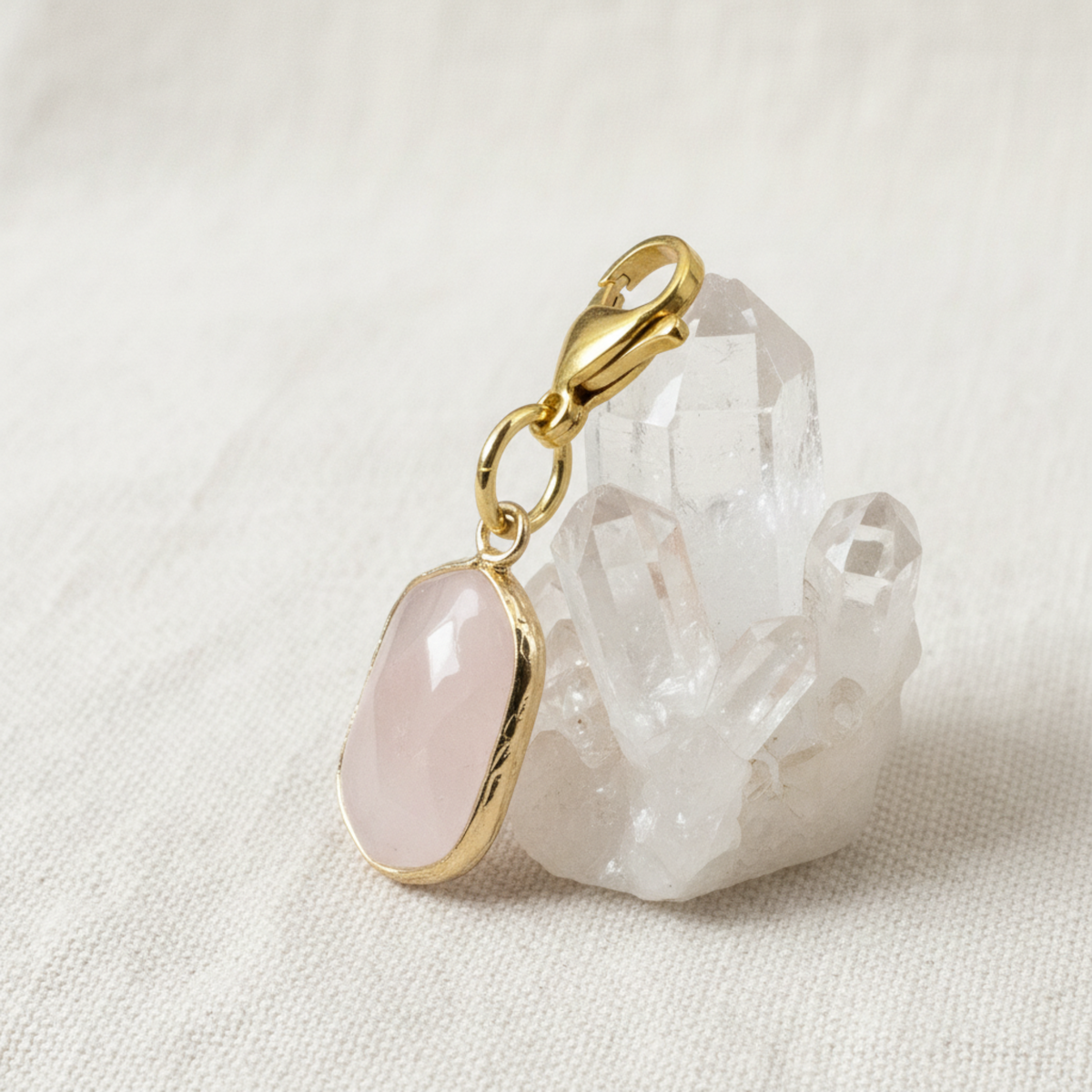 Hackberry Creek faceted oval rose quartz charm with gold-plated brass lobster clasp resting on a clear quartz crystal
