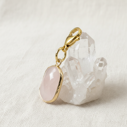 Hackberry Creek faceted oval rose quartz charm with gold-plated brass lobster clasp resting on a clear quartz crystal