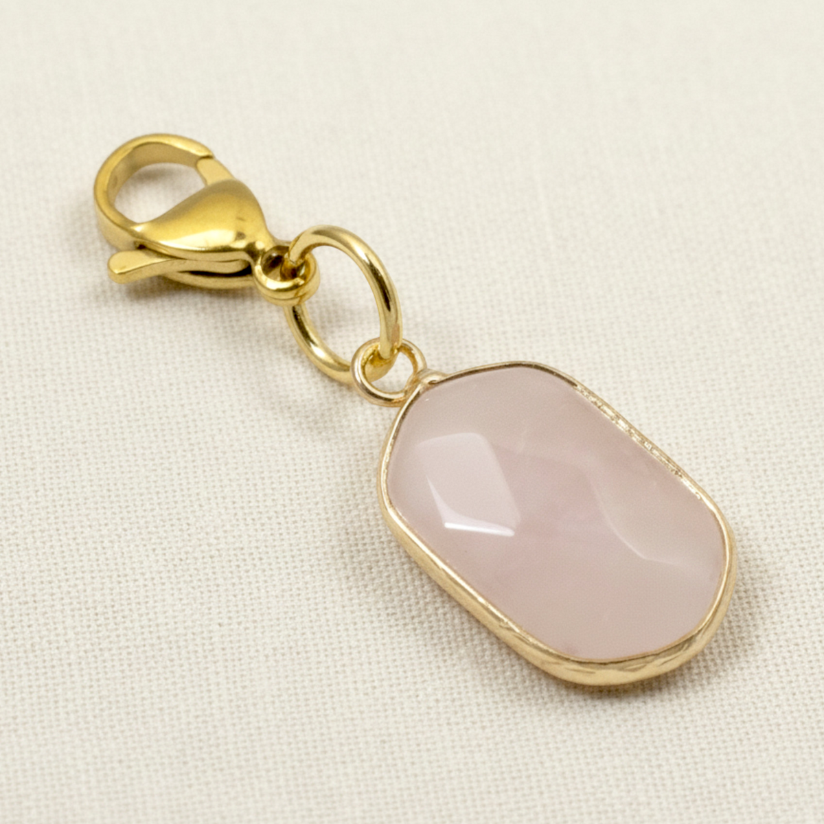 Hackberry Creek faceted light pink rose quartz charm with gold-plated brass lobster clasp on a textured white fabric
