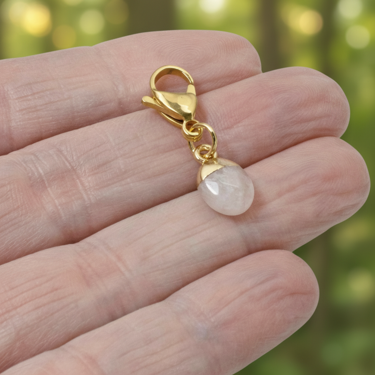 Hackberry Creek dainty oval rose quartz charm with a gold-plated stainless steel clasp held in a hand