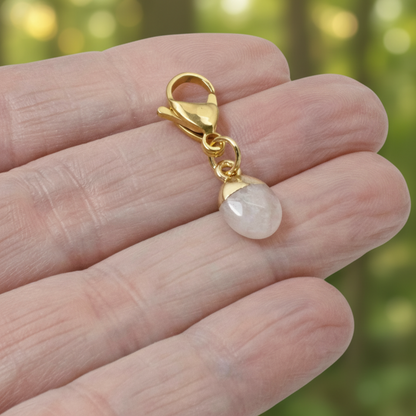 Hackberry Creek dainty oval rose quartz charm with a gold-plated stainless steel clasp held in a hand