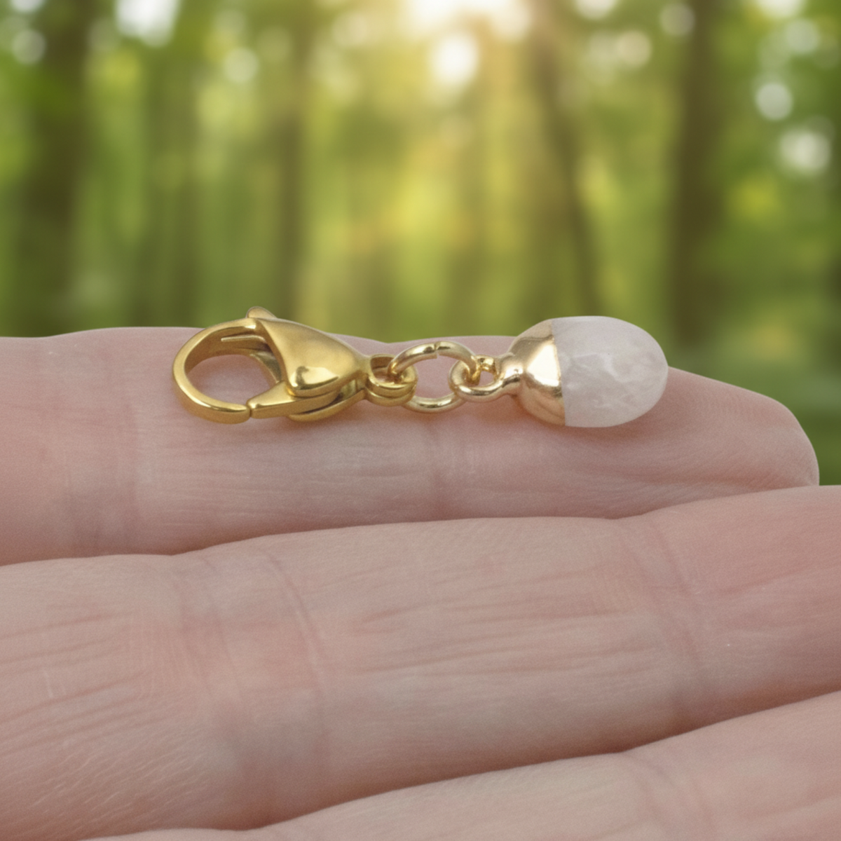Hackberry Creek dainty oval rose quartz charm with a gold-plated stainless steel clip-on clasp held in a palm.