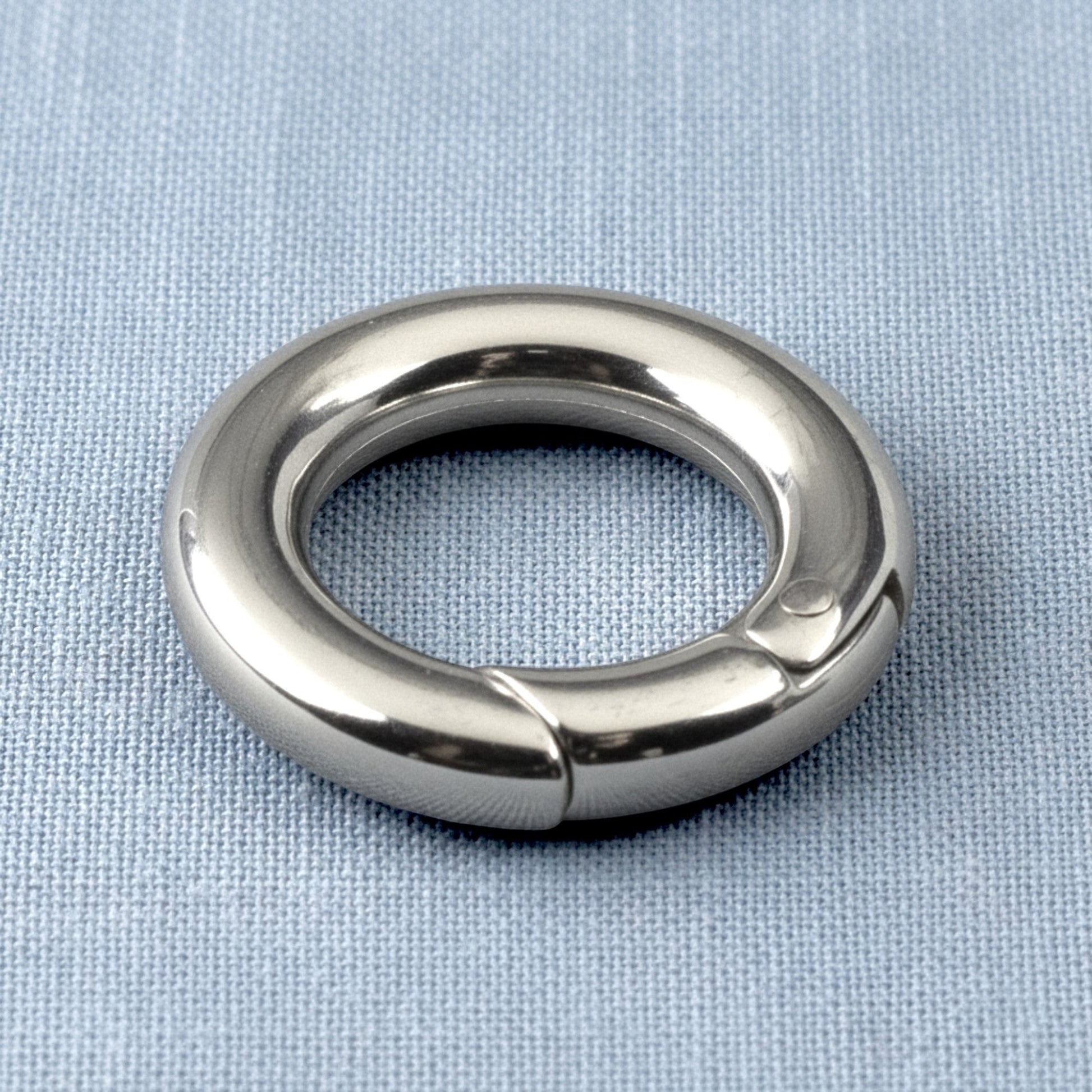 Hackberry Creek 15mm round stainless steel carabiner spring clasp with a polished silver finish on a blue fabric base.