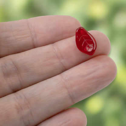 Hackberry Creek transparent Siam red Czech glass leaf bead with veining detail held on a fingertip