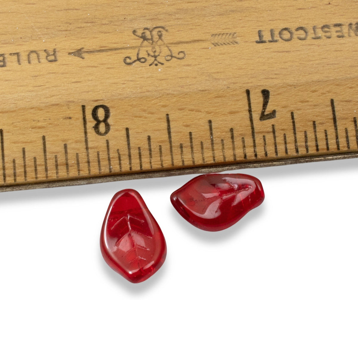 Hackberry Creek transparent Siam red Czech glass leaf beads with veining detail next to a ruler for scale