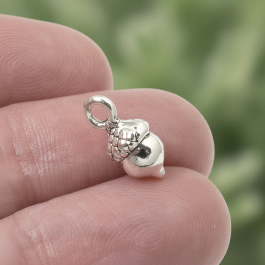 Hackberry Creek tiny antique silver acorn charm held between fingers, showing textured cap and 3D detail.