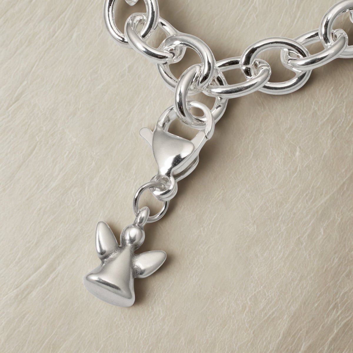 Hackberry Creek silver angel charm with lobster clasp attached to a silver chain on a textured beige background.