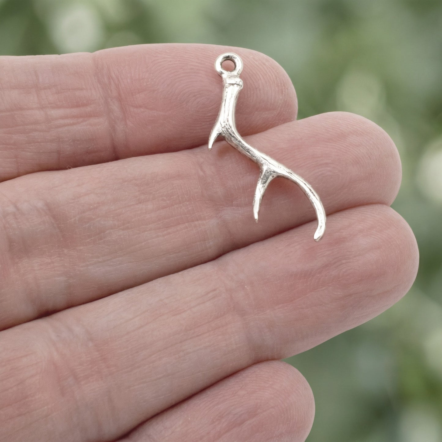 Hackberry Creek silver plated pewter antler charm held in hand for jewelry making