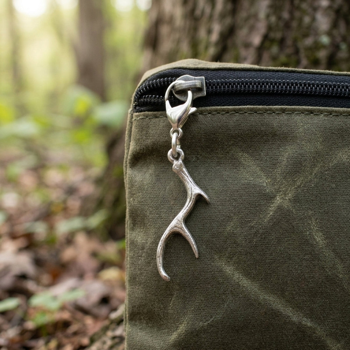Hackberry Creek silver antler clip-on charm attached to a green canvas bag zipper in a forest setting