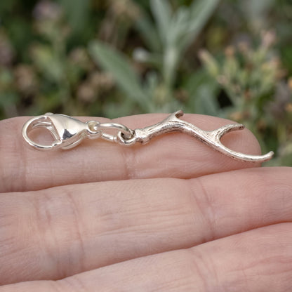 Hackberry Creek silver antler clip-on charm with a lobster clasp held in a hand against a blurred garden background