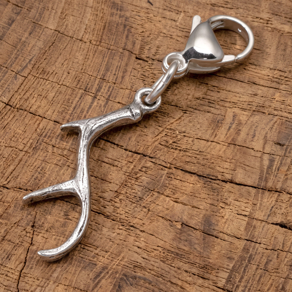 Hackberry Creek silver antler clip-on charm with a lobster clasp, resting on a rustic wooden surface.