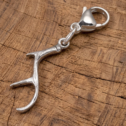 Hackberry Creek silver antler clip-on charm with a lobster clasp, resting on a rustic wooden surface.