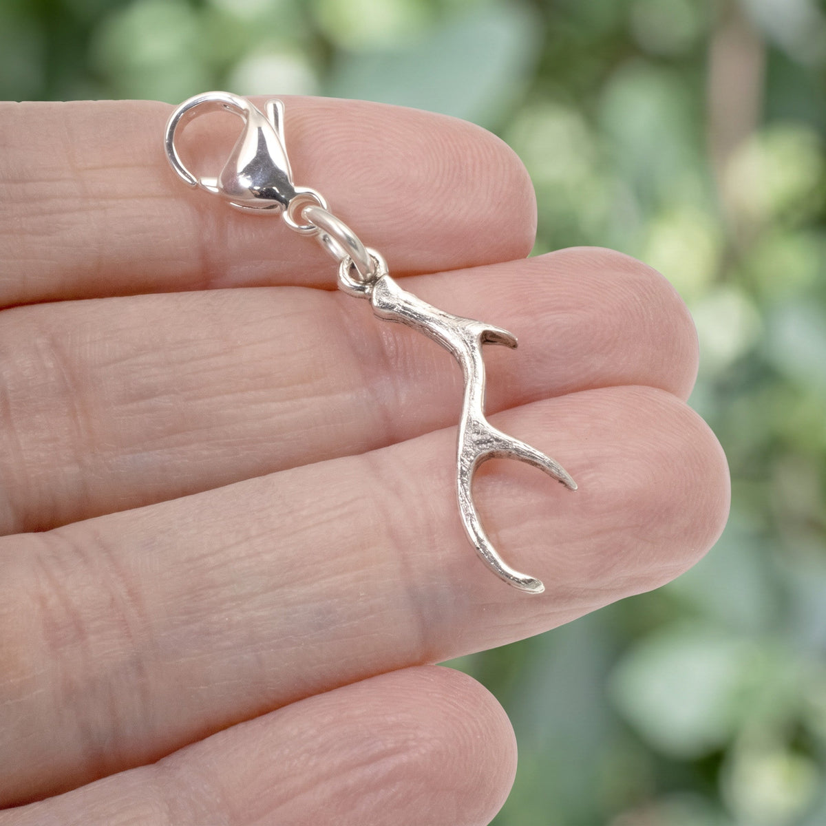 Hackberry Creek silver antler clip-on charm held in hand, featuring a detailed woodland design with a lobster clasp.