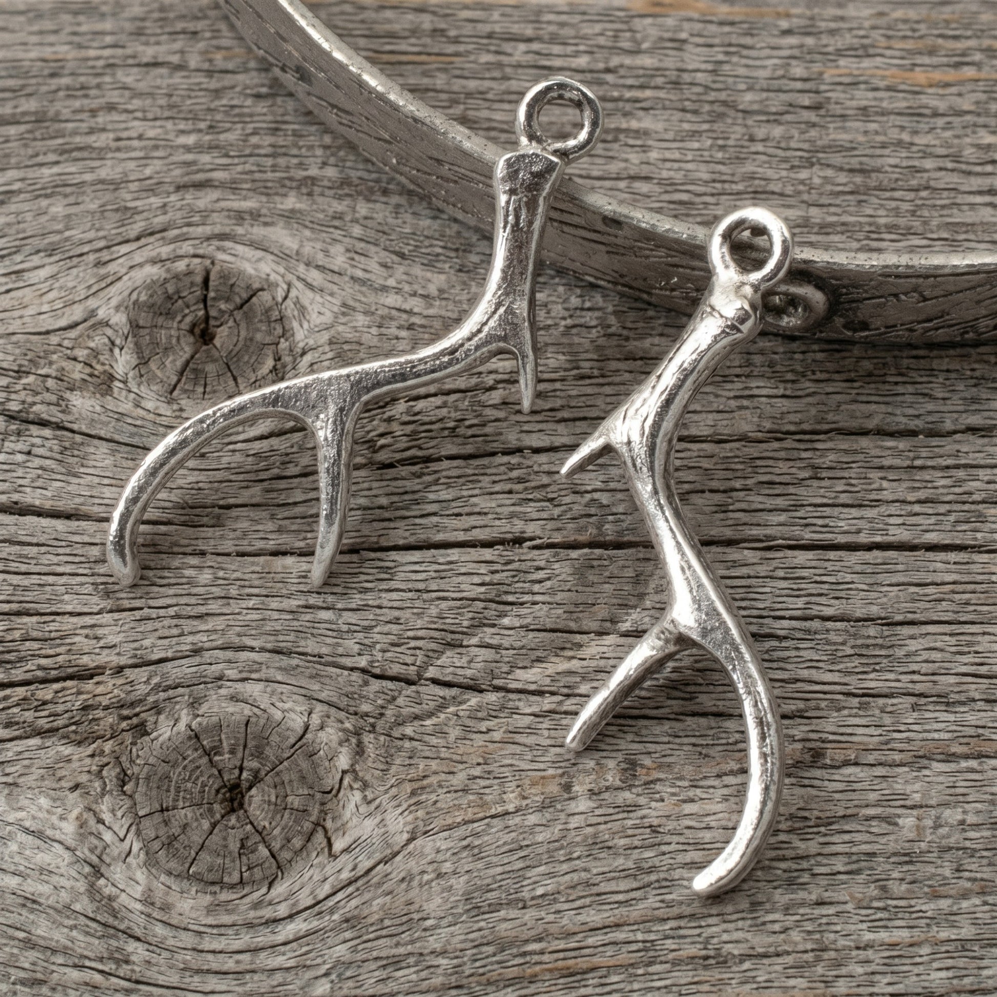 Hackberry Creek Nunn Design silver plated pewter antler charms for artisan jewelry making on a rustic wood background.