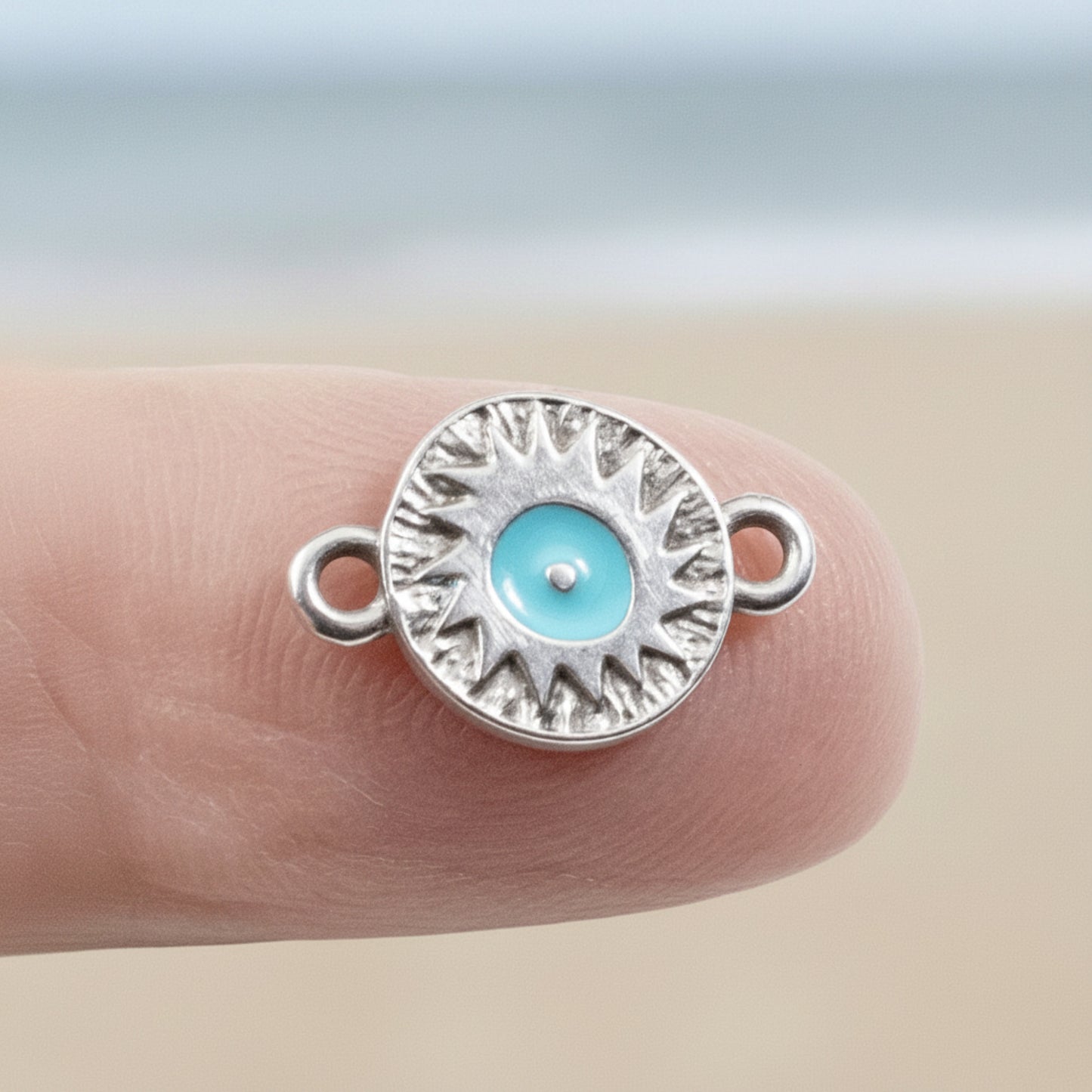 Hackberry Creek antique silver evil eye connector charm with a vibrant aqua enamel center held on a fingertip.