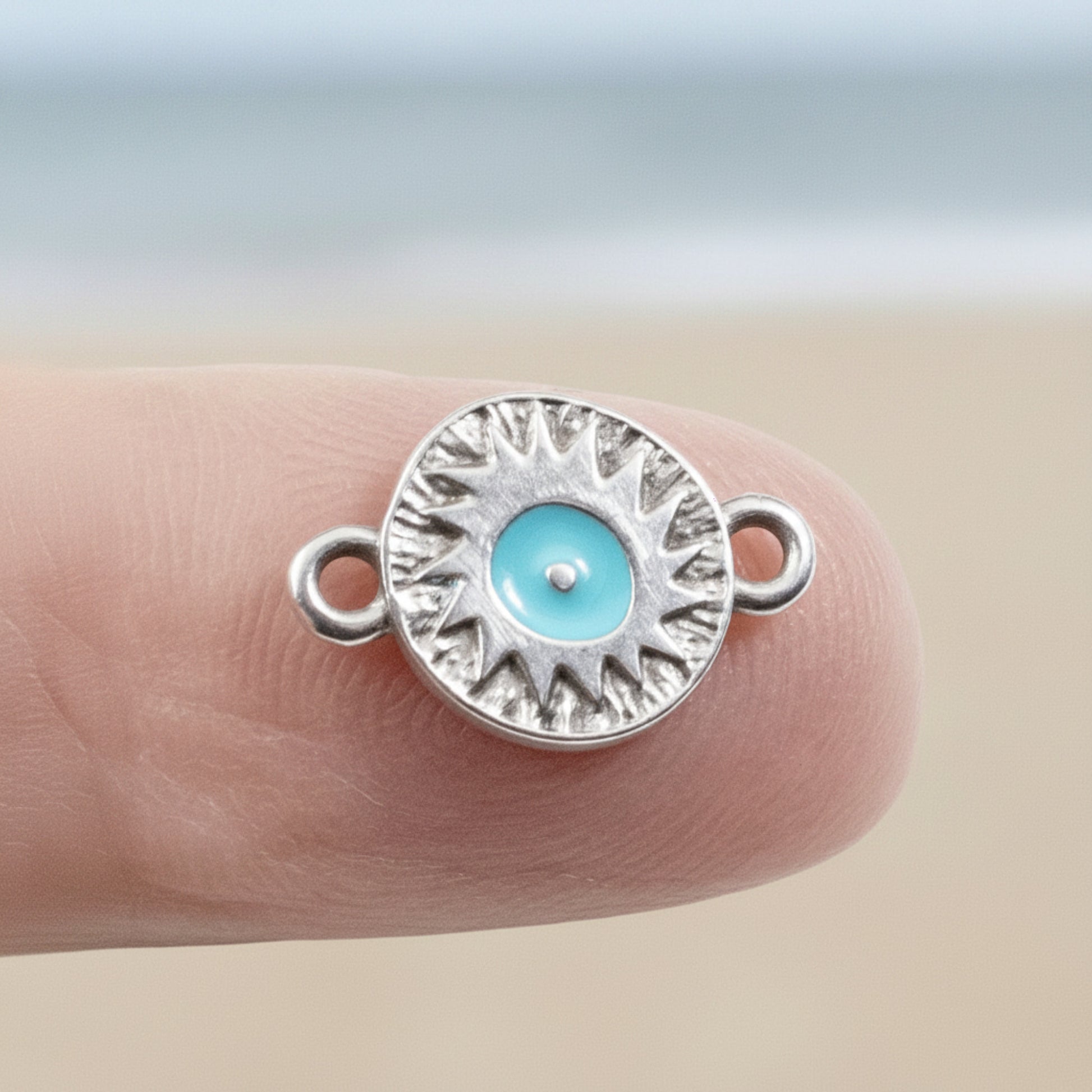 Hackberry Creek antique silver evil eye connector charm with a vibrant aqua enamel center held on a fingertip.