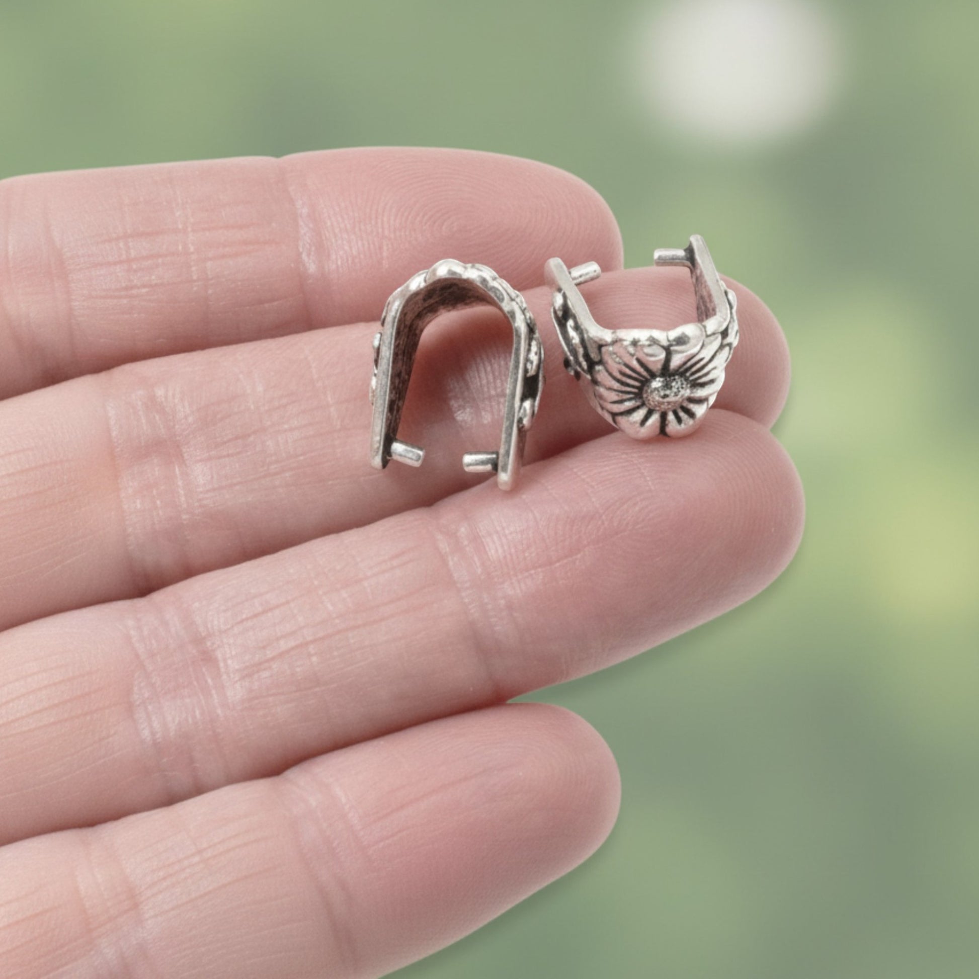 Hackberry Creek TierraCast silver pinch bails with antique floral vine design held in a hand for jewelry making