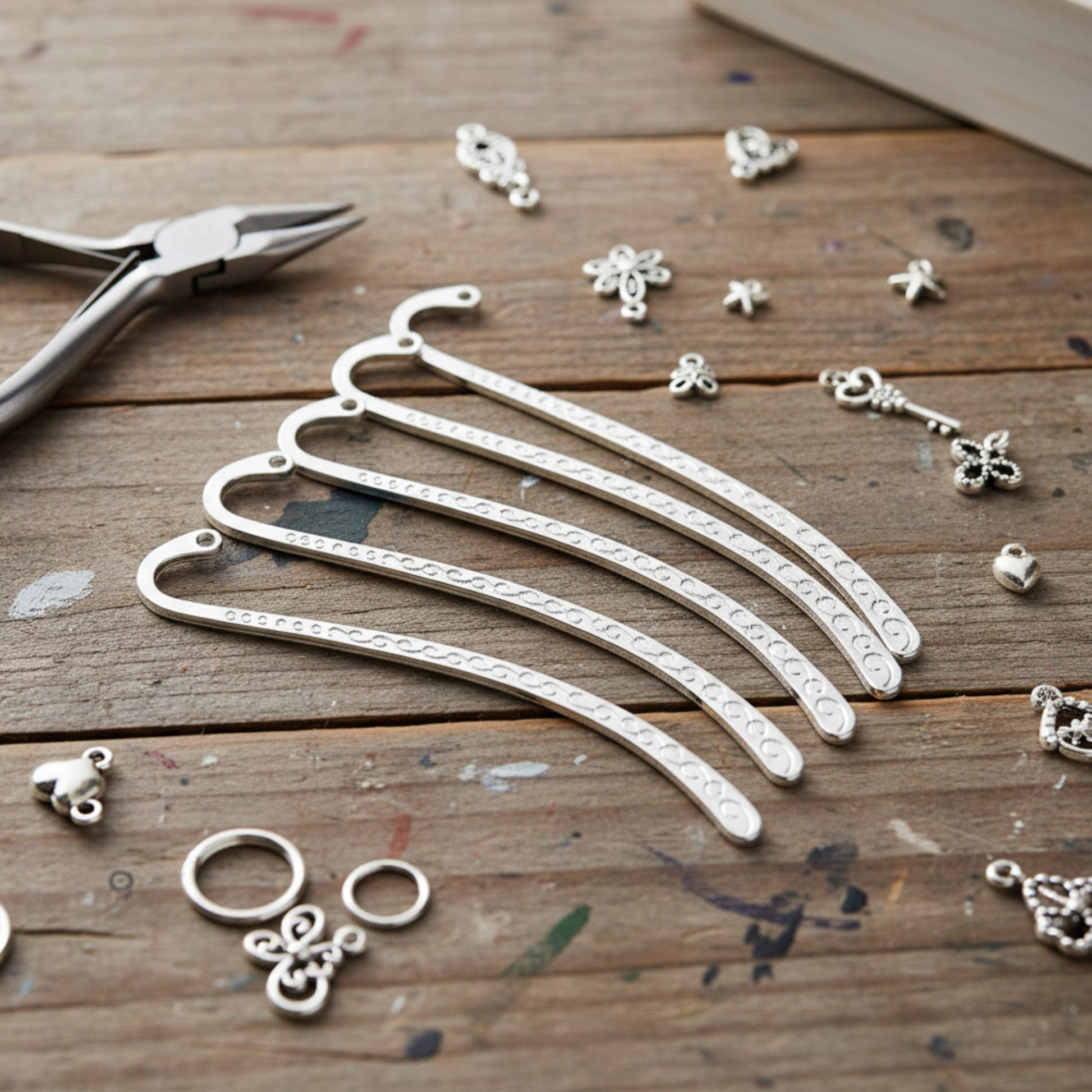 Hackberry Creek silver-tone metal hook bookmark blanks with swirl patterns, arranged on a rustic wooden craft table.