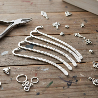 Hackberry Creek silver-tone metal hook bookmark blanks with swirl patterns, arranged on a rustic wooden craft table.