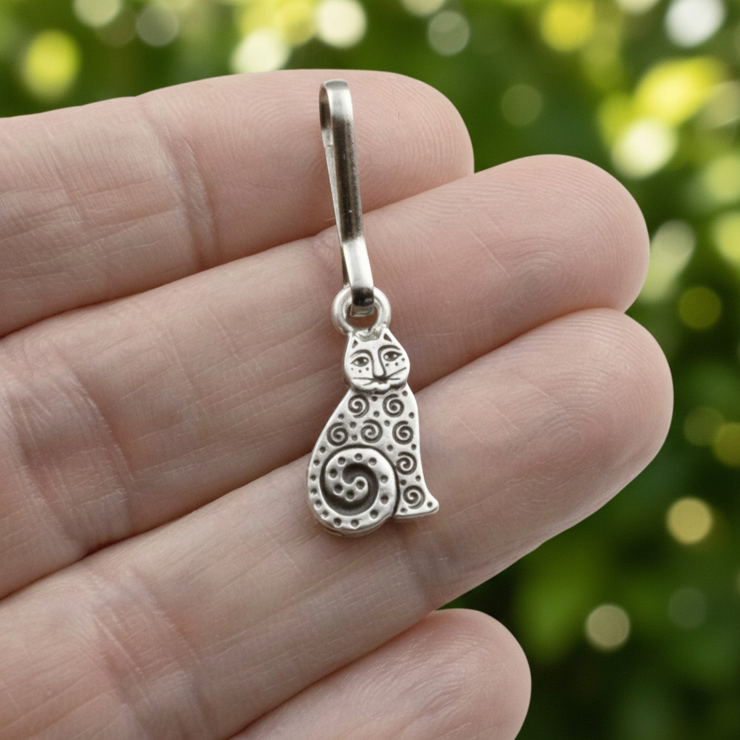 Hackberry Creek silver-plated pewter sitting cat zipper charm with intricate spiral details held in a hand.