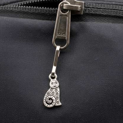 Hackberry Creek silver-plated pewter sitting cat zipper charm with intricate spiral details attached to a black bag.