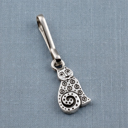 Hackberry Creek silver-plated pewter sitting cat zipper charm with intricate spiral detailing on a blue fabric background.