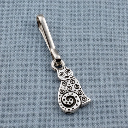 Hackberry Creek silver-plated pewter sitting cat zipper charm with intricate spiral detailing on a blue fabric background.