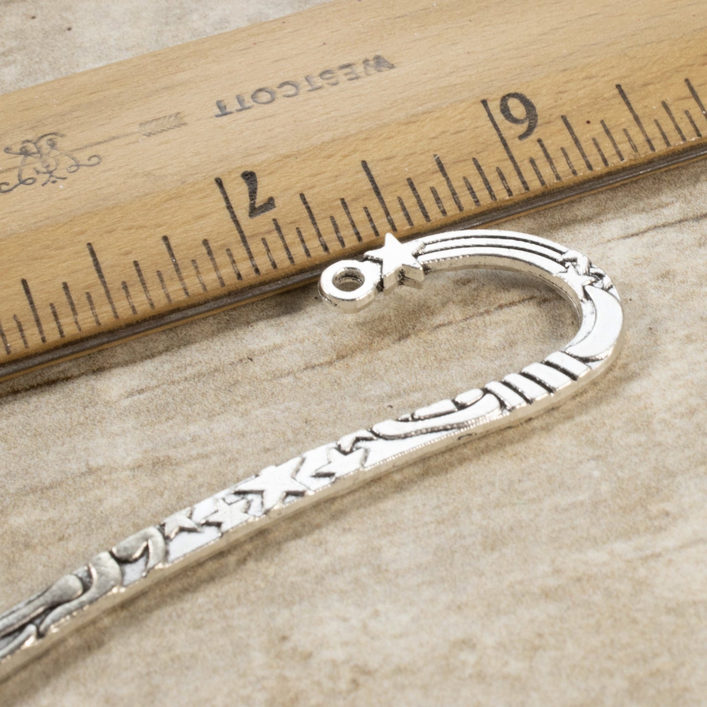 Hackberry Creek antique silver zinc alloy hook bookmark with celestial star and sun design next to a wooden ruler.