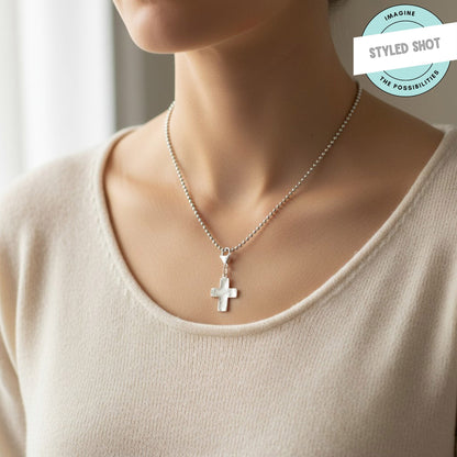 Hackberry Creek silver distressed cross charm worn as a necklace pendant on a ball chain against a cream top