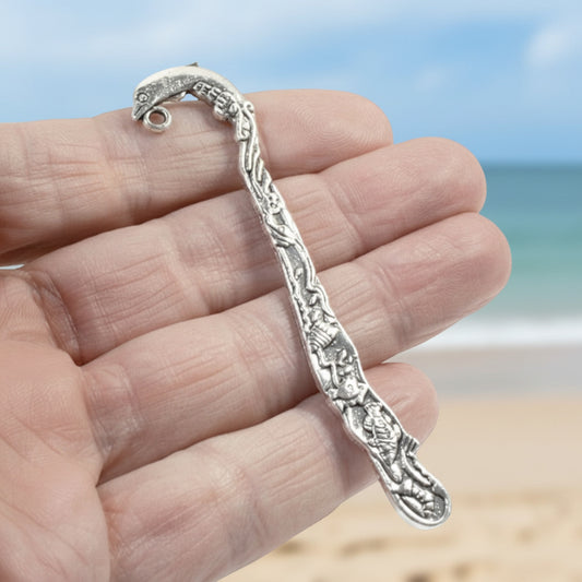 Hackberry Creek antique silver dolphin bookmark with beach-themed engraving held in hand against a blurred beach background