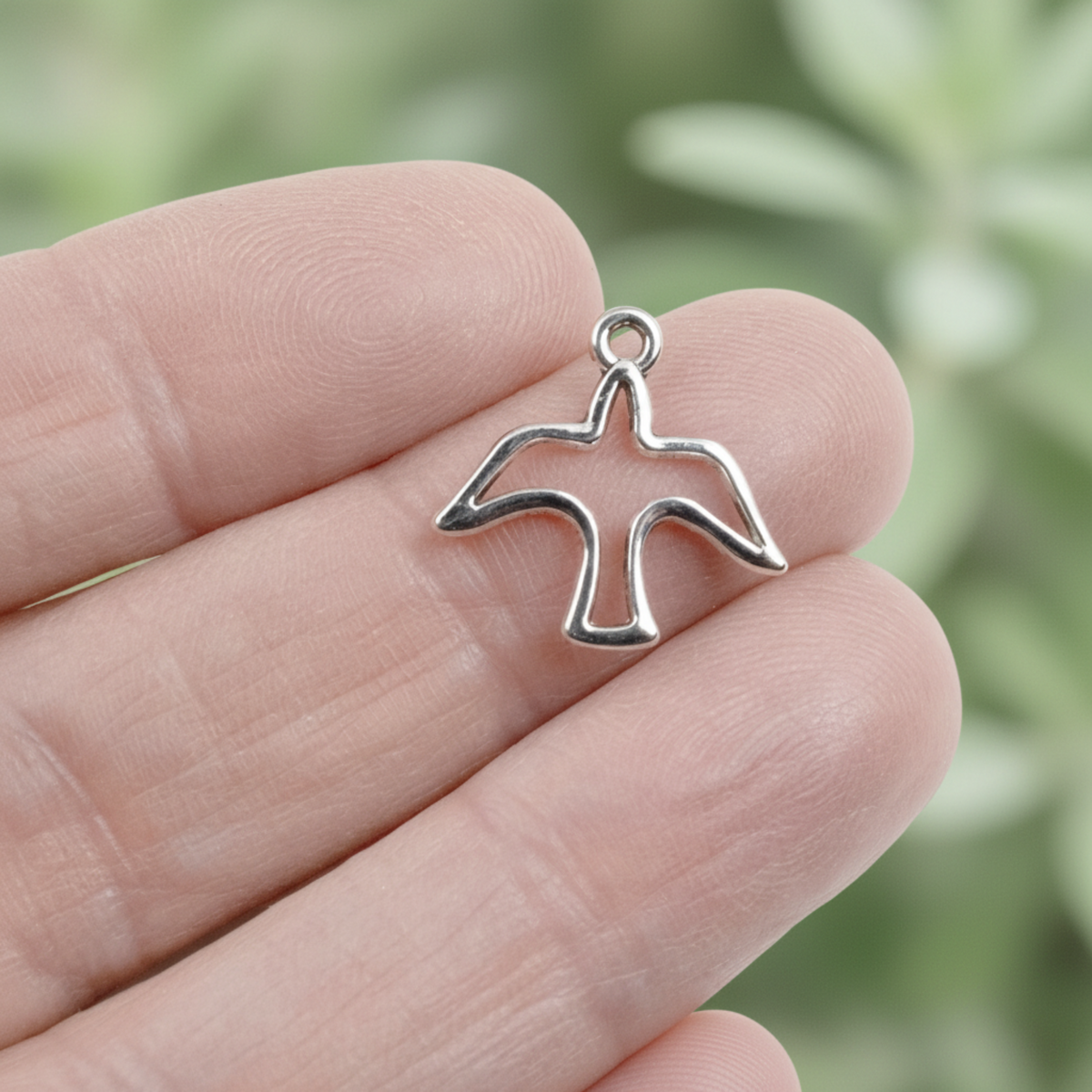 Hackberry Creek silver peace dove charm with an open silhouette design held between fingers