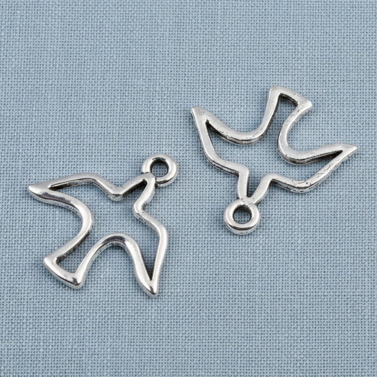 Hackberry Creek silver peace dove charms with an open silhouette design for jewelry making on a blue fabric background