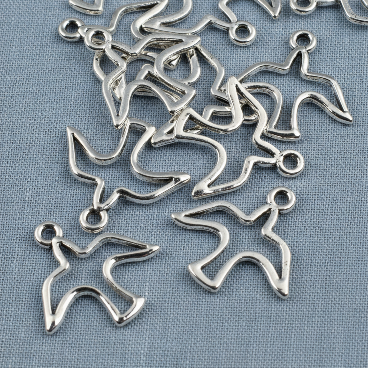 Hackberry Creek silver peace dove charms with an open silhouette design for jewelry making on a blue fabric background