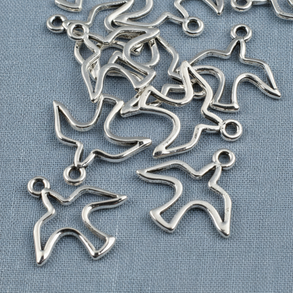 Hackberry Creek silver peace dove charms with an open silhouette design for jewelry making on a blue fabric background