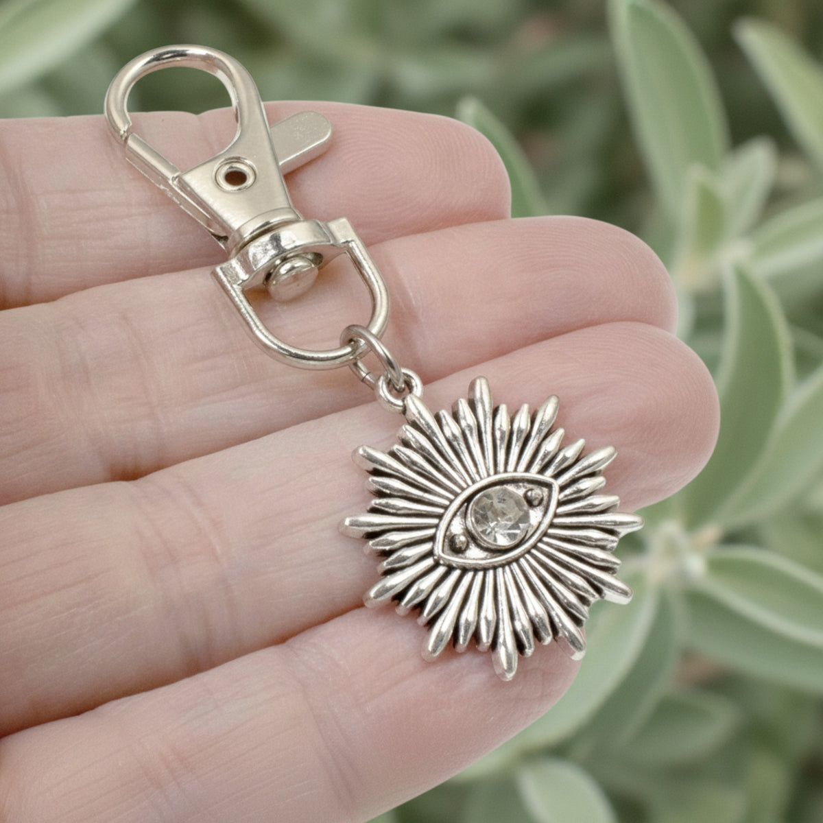 Hackberry Creek silver metal alloy evil eye sunburst bag charm with a clear rhinestone accent on a lobster clasp.