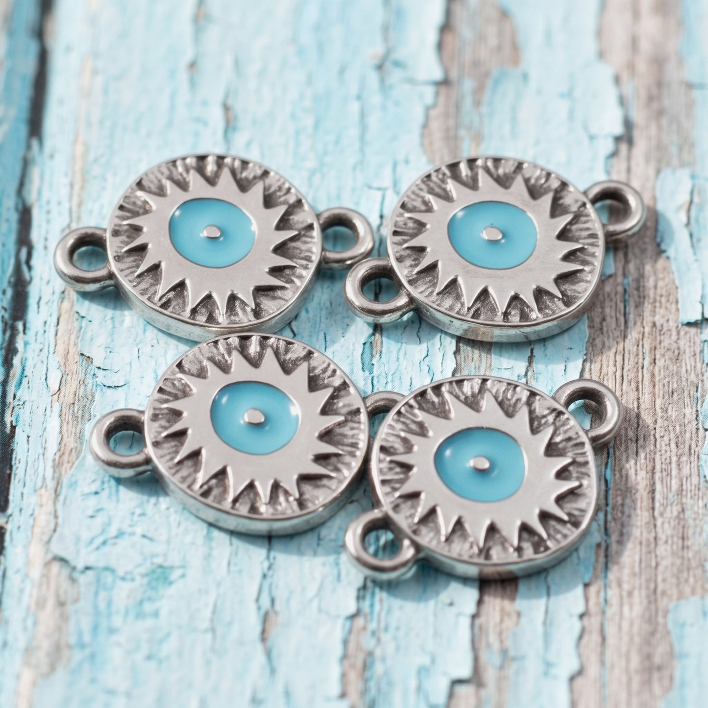 Hackberry Creek antique silver evil eye connector charms with vibrant aqua enamel centers on a rustic blue wood surface.