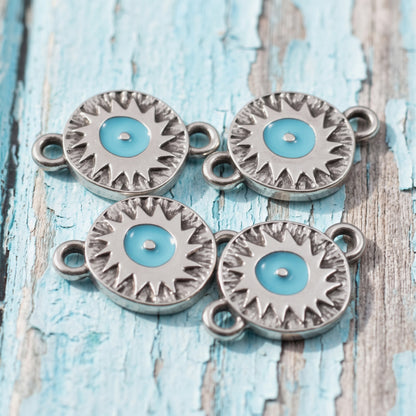 Hackberry Creek antique silver evil eye connector charms with vibrant aqua enamel centers on a rustic blue wood surface.