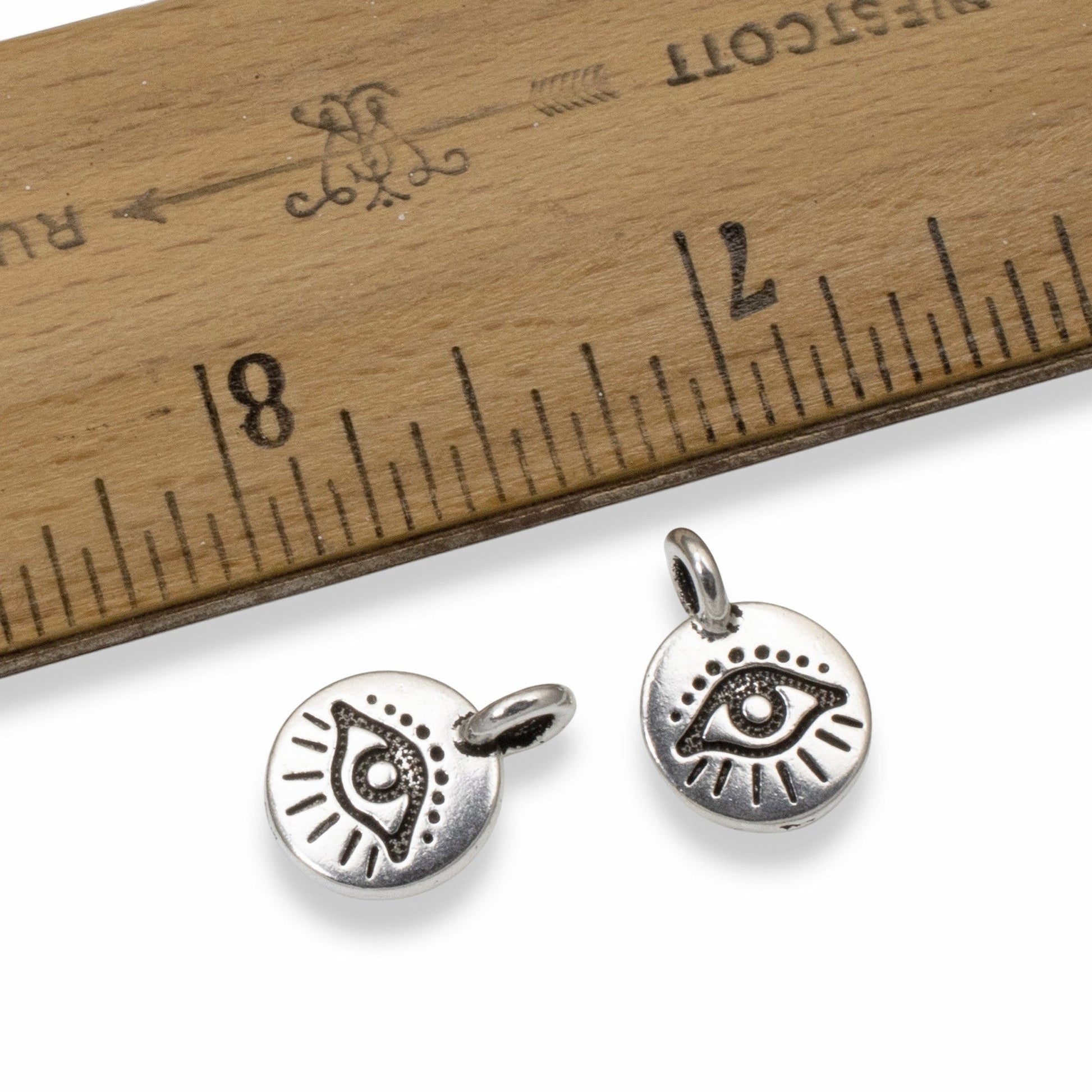 Hackberry Creek silver plated pewter evil eye charms with antique finish and horizontal bail next to a wooden ruler.