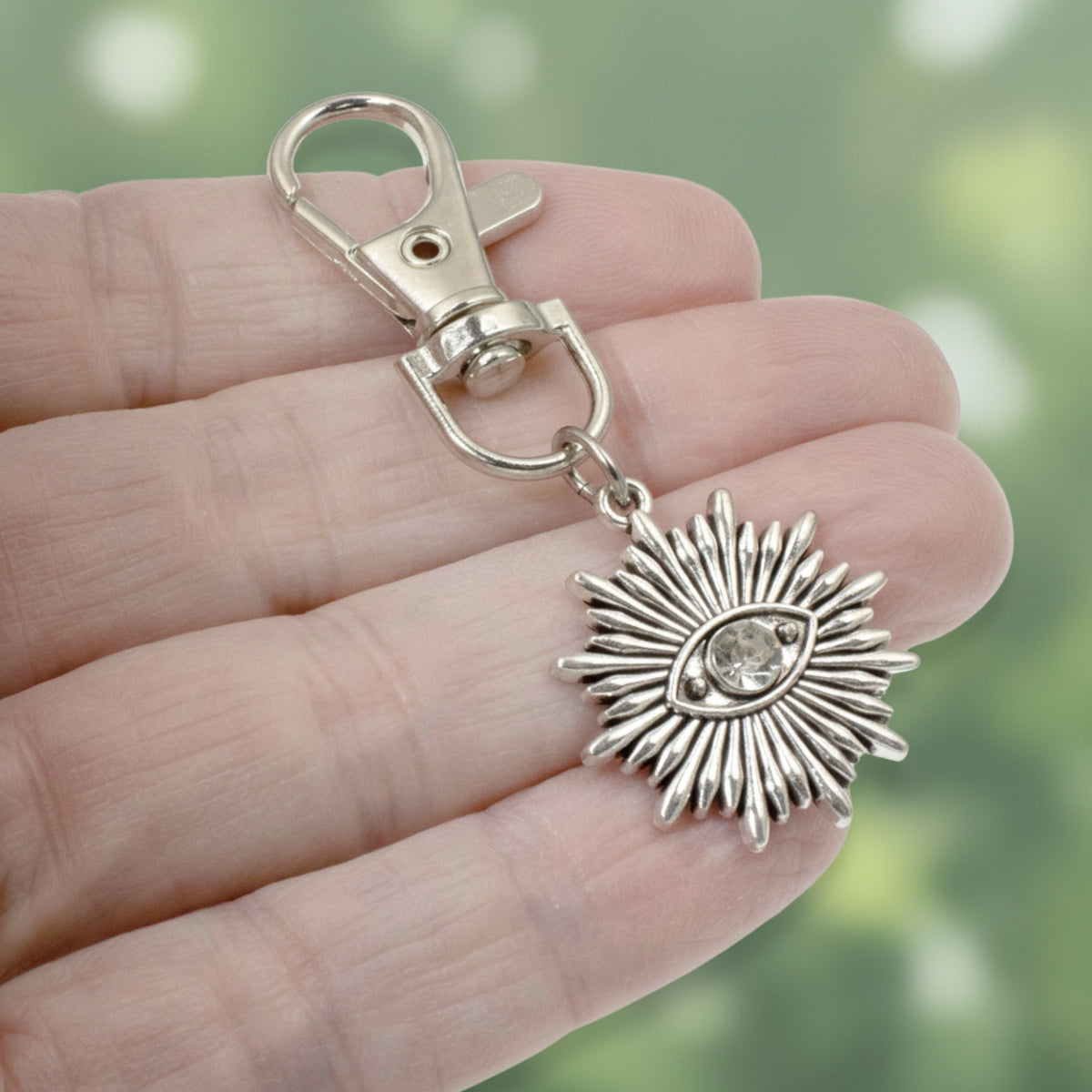 Hackberry Creek silver sunburst evil eye key fob charm with a clear rhinestone center held in a hand