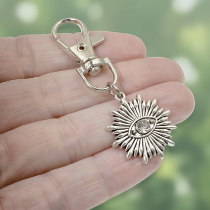 Hackberry Creek silver sunburst evil eye key fob charm with a clear rhinestone center held in a hand