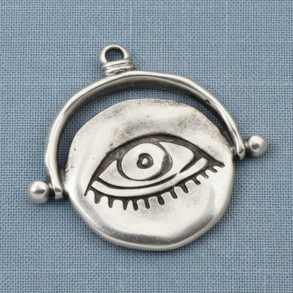 Hackberry Creek silver plated evil eye pendant with a hand-formed organic texture on a blue fabric background.